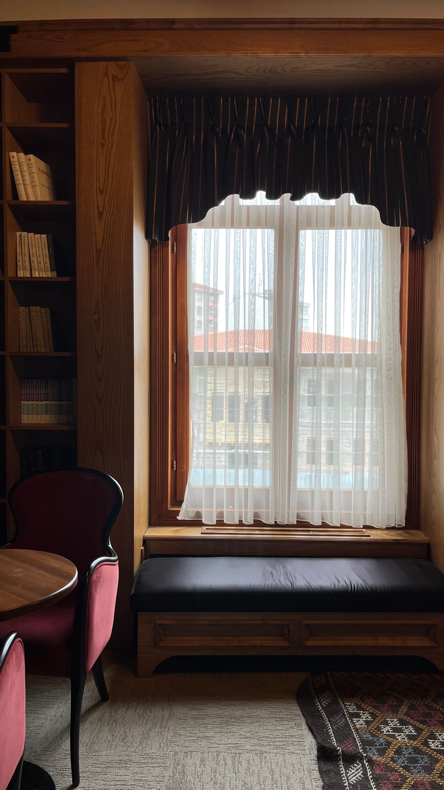 Window-adjacent upholstered bench in a warm room filled with books
