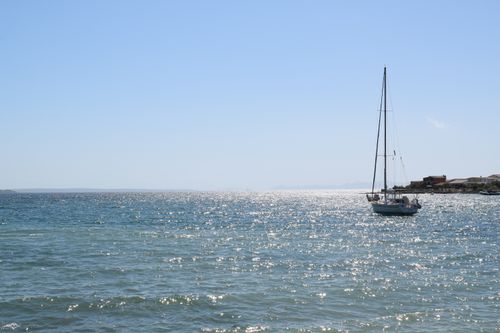 Free A peaceful sailboat on a sunny day, gliding over the sparkling blue sea with clear skies above. Stock Photo