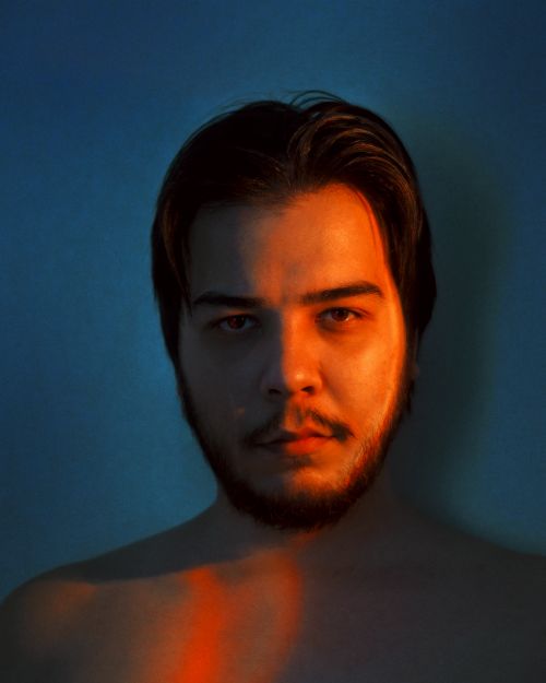 Free Portrait of an adult male with short hair against a blue background, highlighted by creative lighting. Stock Photo