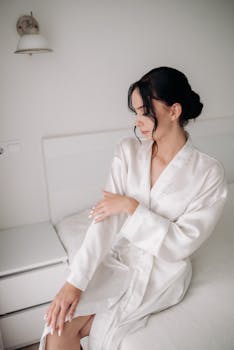 Stylish woman in a white silk bathrobe sitting elegantly on a bed, perfect for fashion and lifestyle themes.
