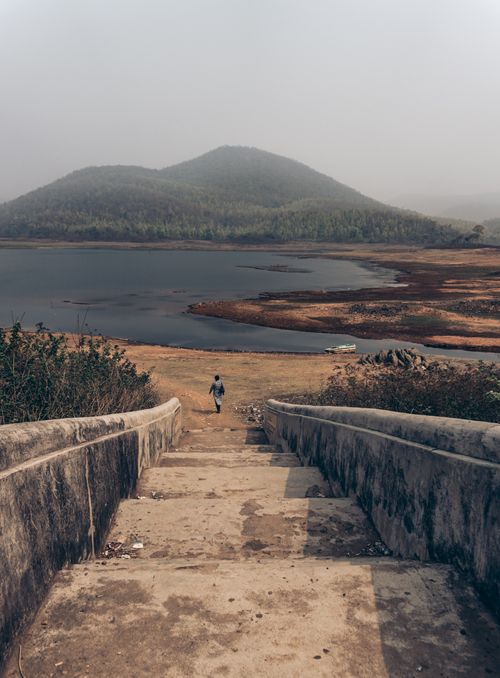 Free A peaceful scene of a person walking down steps towards a fog-covered lake and hills. Stock Photo