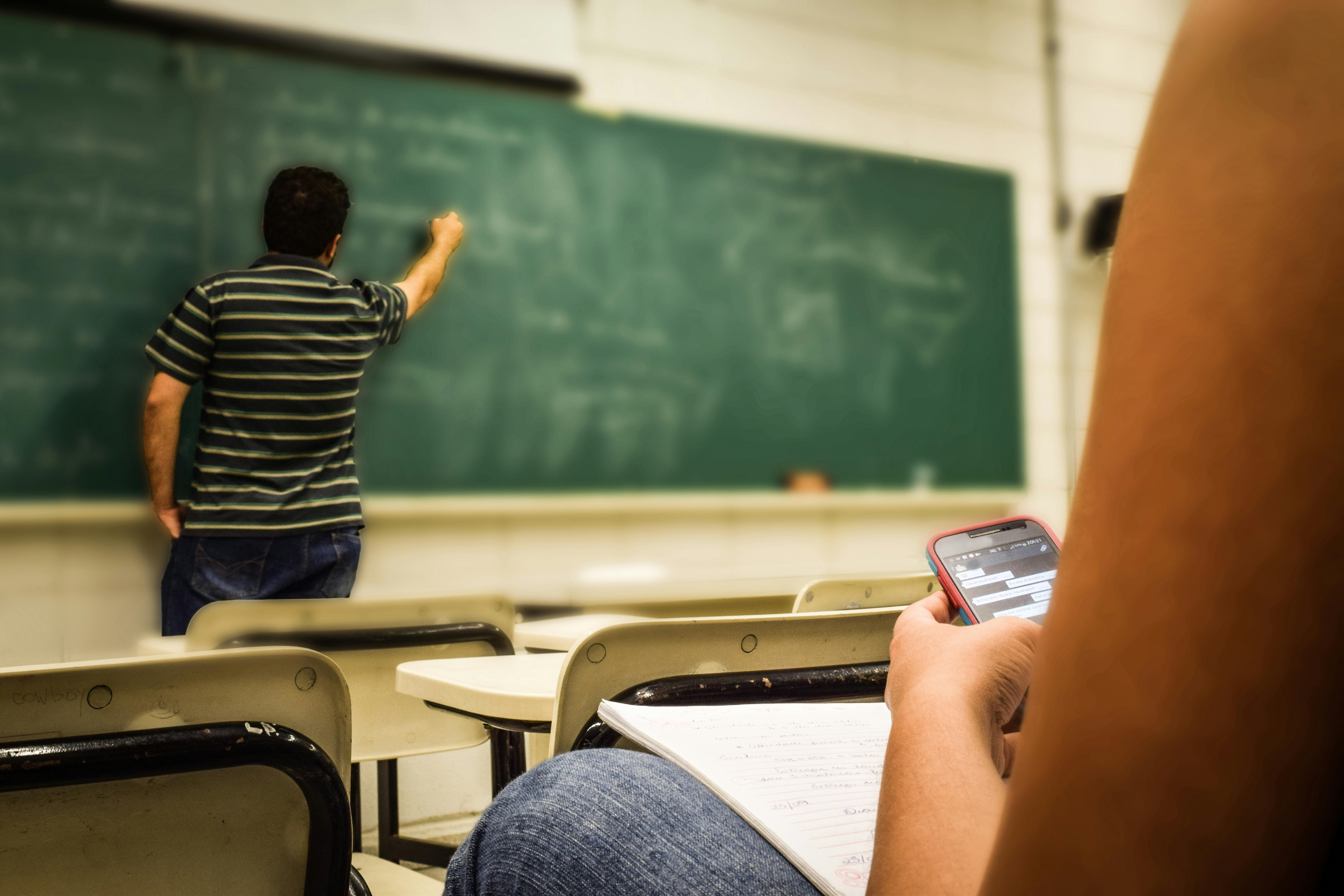 Man writing on a blackboard in a classroom | Photo: Pexels