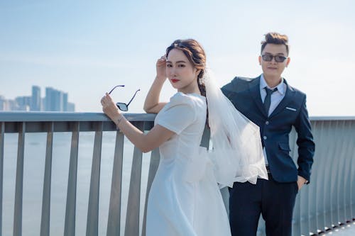 Bride and Groom in Sunglasses Standing on the Bridge Overlooking the City 