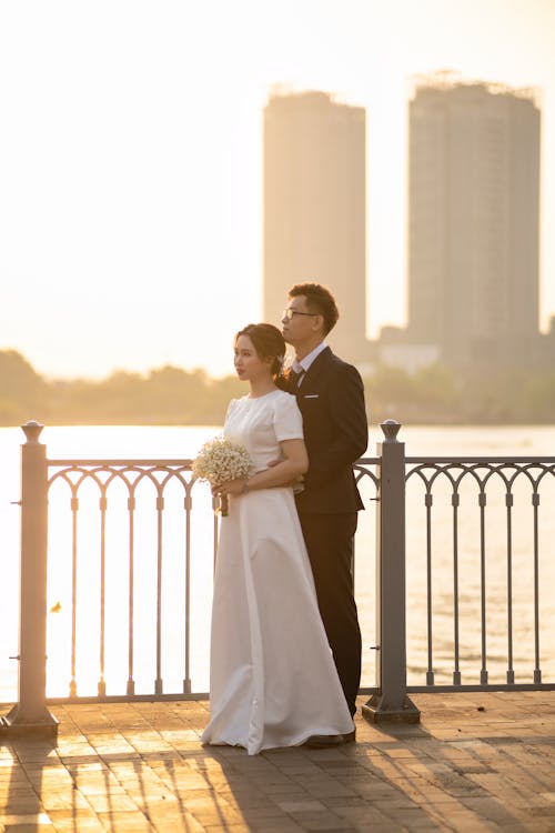 Bride and Groom Standing on a Pier overlooking the City at Sunset 