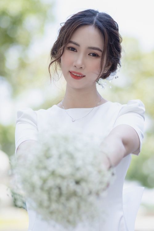 Free Beautiful bride holding a bouquet, captured in a serene outdoor setting, perfect for wedding themes. Stock Photo