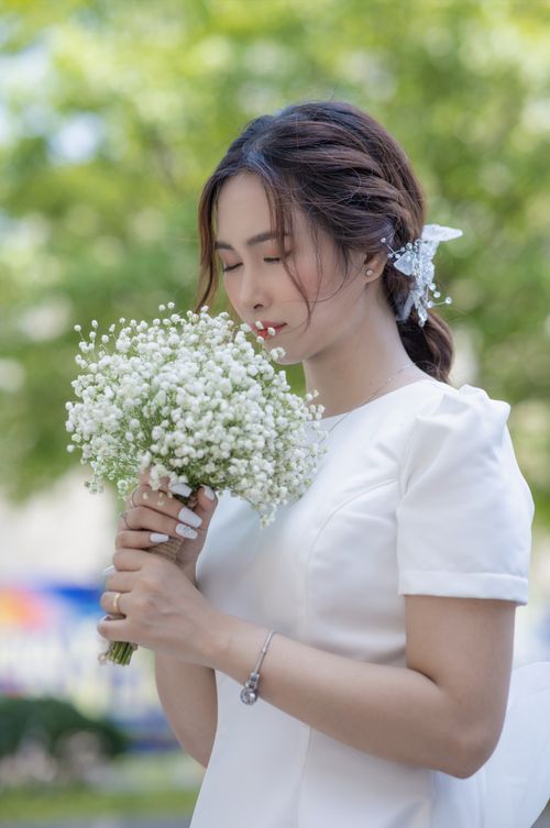 Free A serene bride in a wedding dress enjoys the scent of a white wildflower bouquet outdoors. Stock Photo