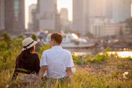 Young Couple Sitting Together on the Grass with a Harbor in the Background