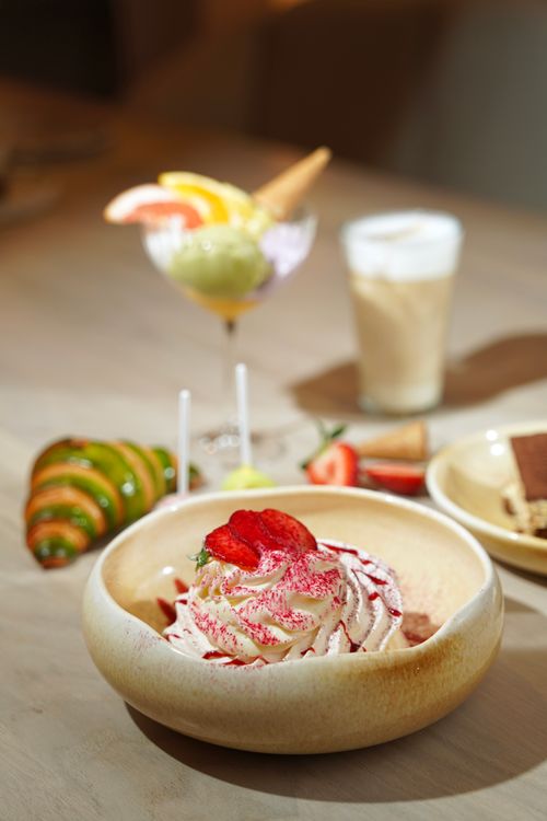 Free Elegant dessert presentation with strawberries, whipped cream, and a variety of sweets in a cozy setting. Stock Photo