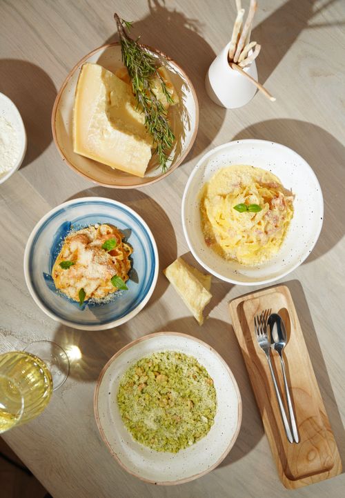 Free An exquisite flat lay of various Italian pasta dishes paired with cheese and herbs on a wooden table. Stock Photo