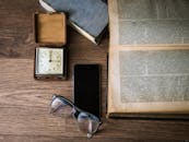 木桌上放着一只老式时钟、一本打开的书、一部智能手机和一副眼镜