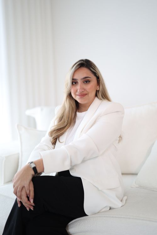 Free Portrait of a smiling woman in a white blazer sitting on a stylish sofa in a minimalist interior. Stock Photo