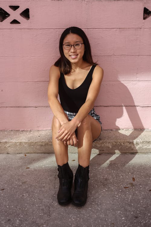 Young Woman Sitting on a Curb by a Pink Wall and Smiling 