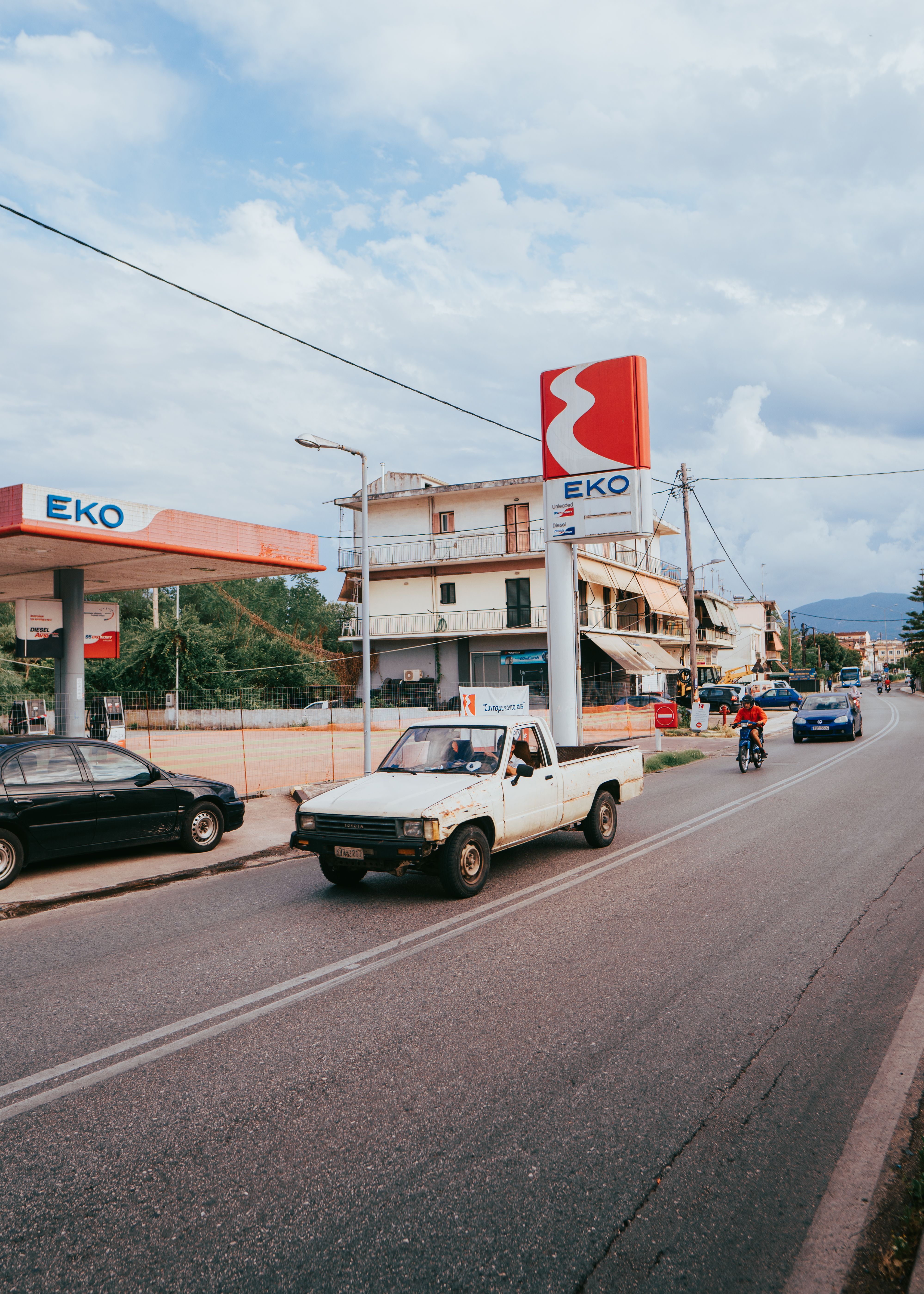 A lively urban street scene with cars and an EKO gas station under a cloudy sky.