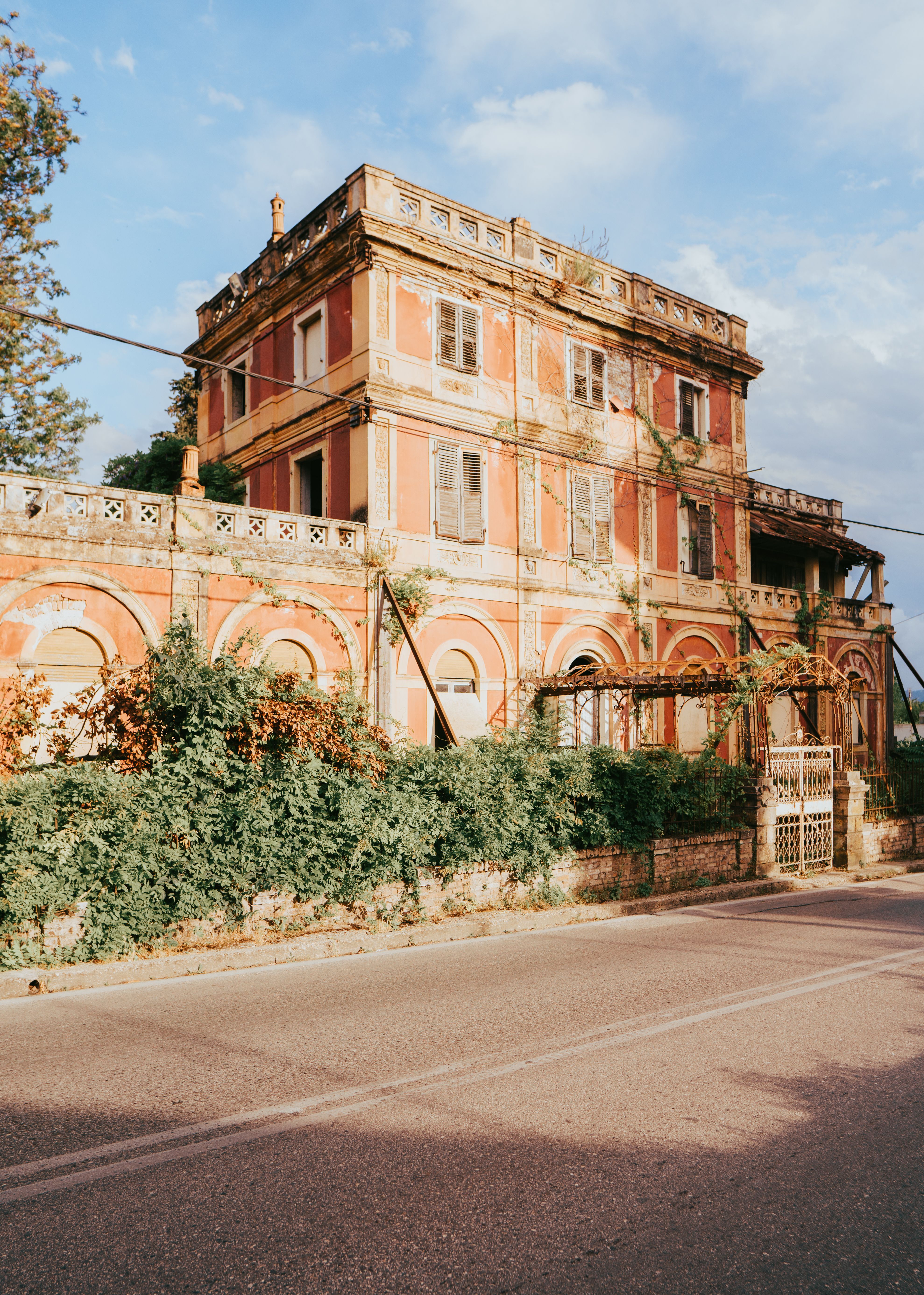 Elegant historic villa in Corfu with a sunlit ivy-covered facade and classic architectural design.