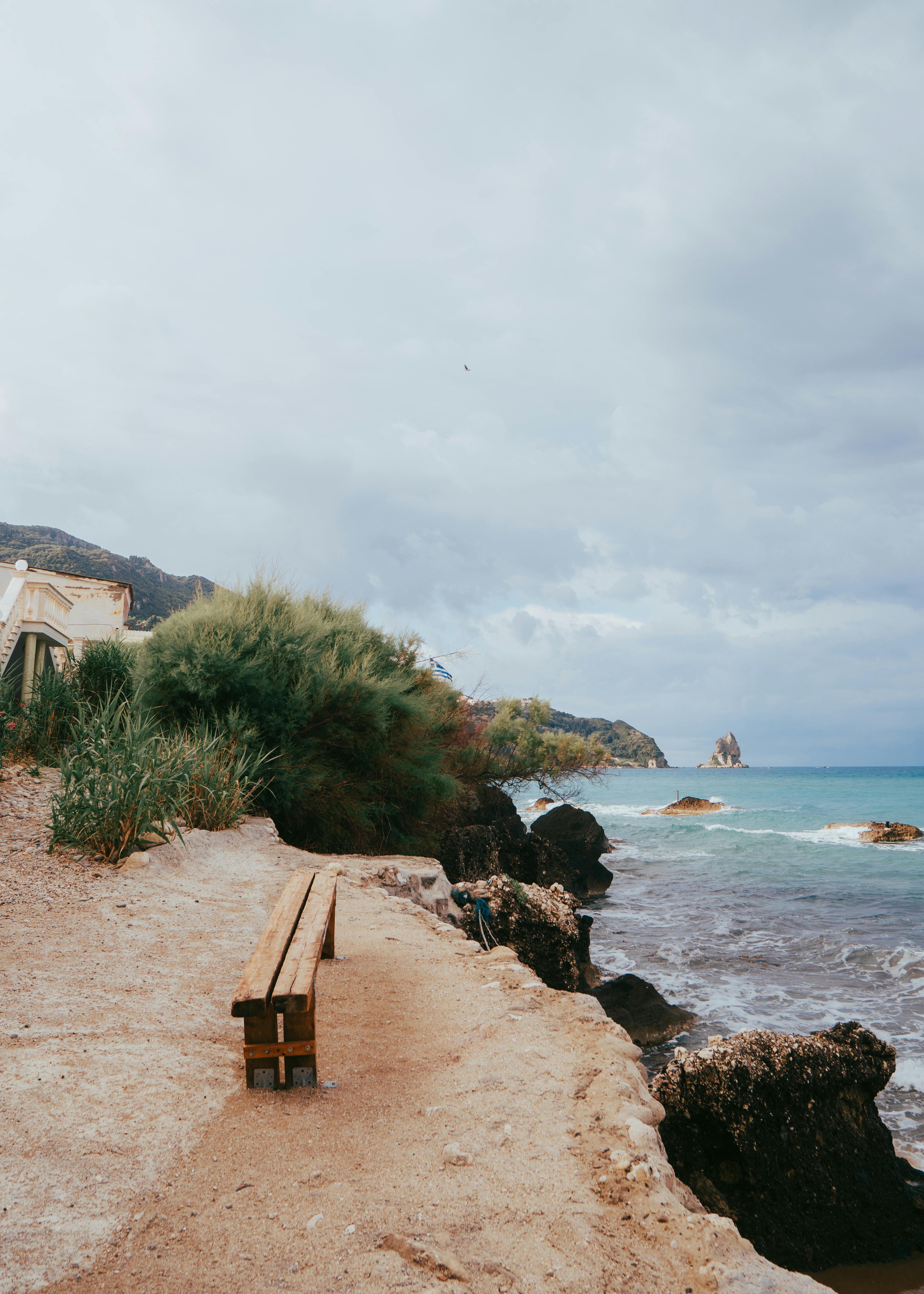 Serene Mediterranean seaside view with a bench overlooking the ocean and rocky coast.