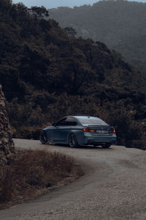 Free A sleek silver car navigates a winding mountain road surrounded by lush greenery. Stock Photo