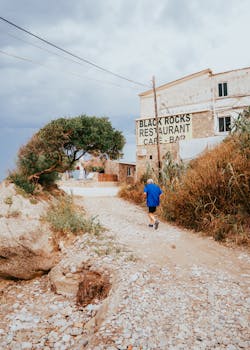 Senior man jogging by a seaside dirt path near a Mediterranean cafe-restaurant.