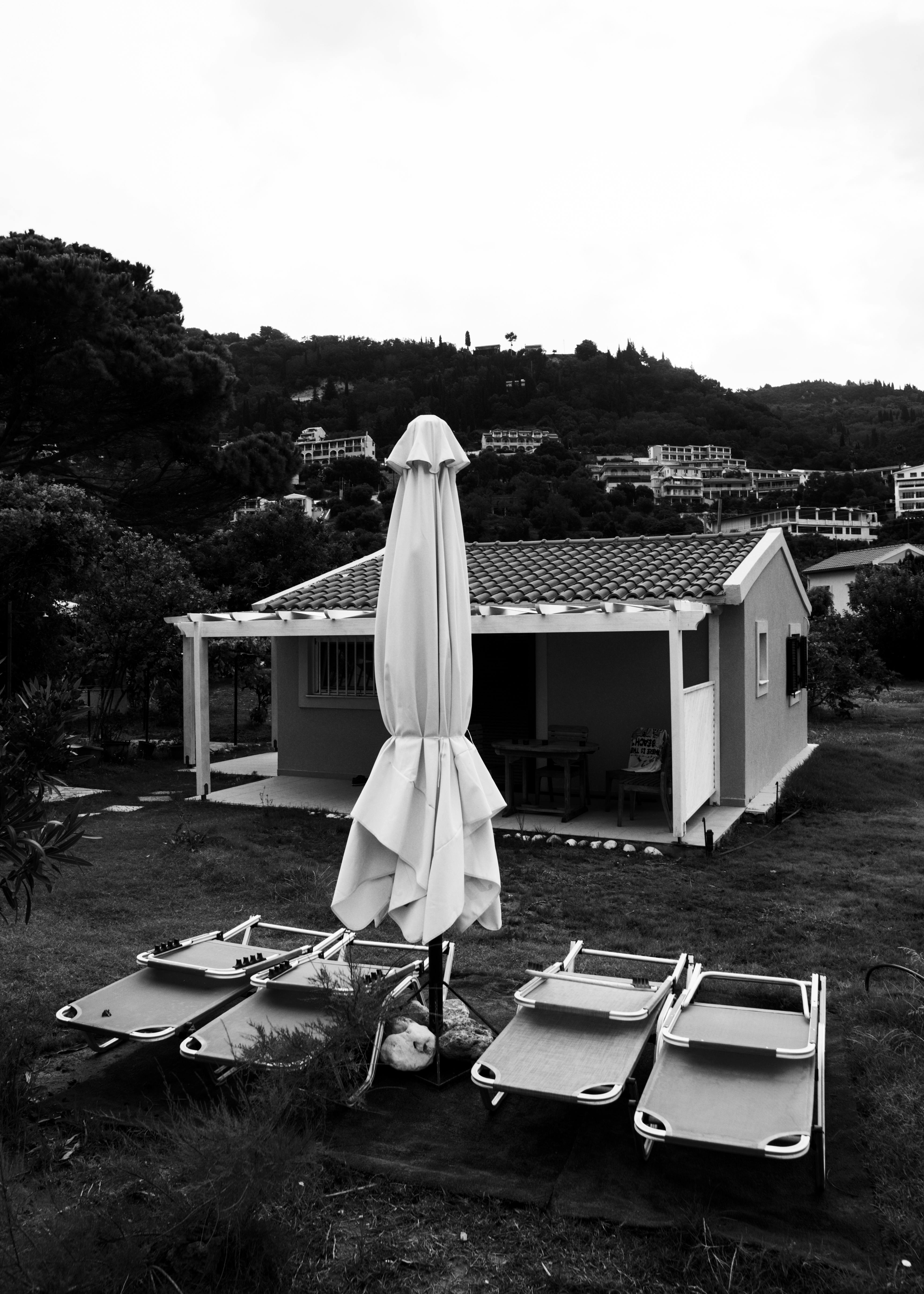 Black and white image of a beachside house with sun loungers and an umbrella.