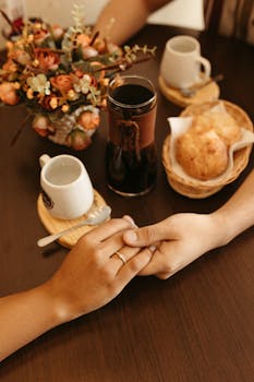A cozy breakfast scene featuring a couple holding hands over coffee and pastries.