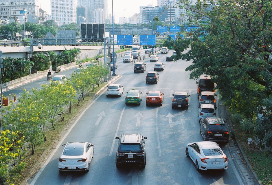 Urban street bustling with cars surrounded by greenery on a sunny day.