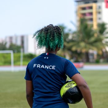 Person with dyed hair in a France football shirt holding a soccer ball outdoors.（イメージ）