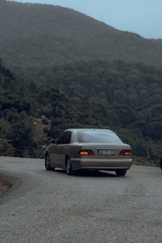 A car drives through a winding mountain road surrounded by dense forest.