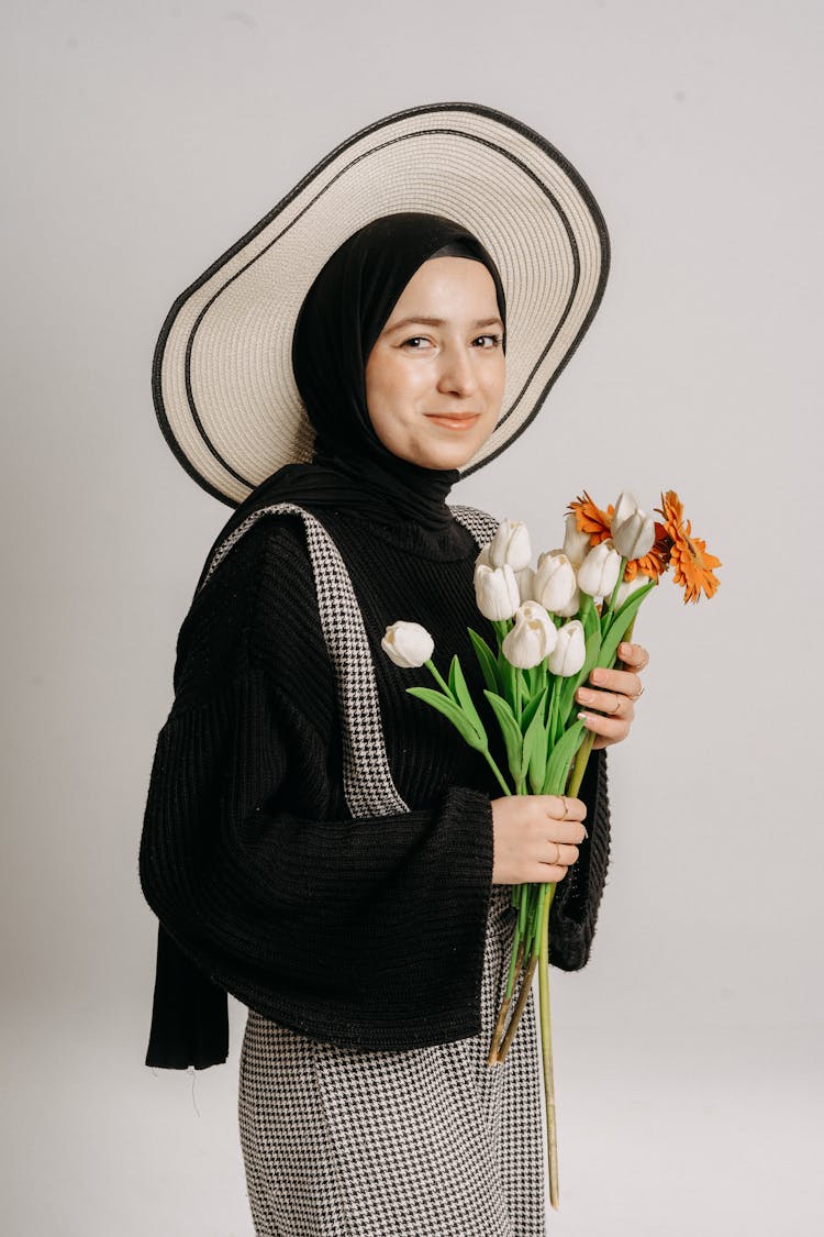 Young Woman In A Hat Holding A Bunch Of Flowers And Smiling 