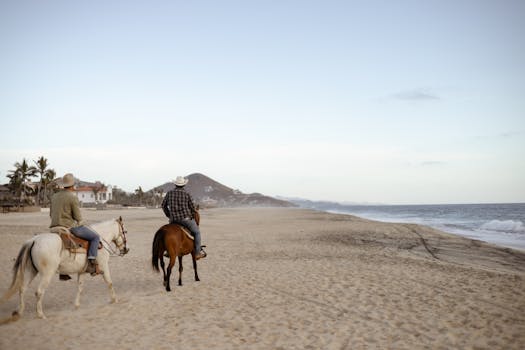 Two people horseback riding along Casa Cyrene Beach, Mexico, capturing serene coastal vibes.