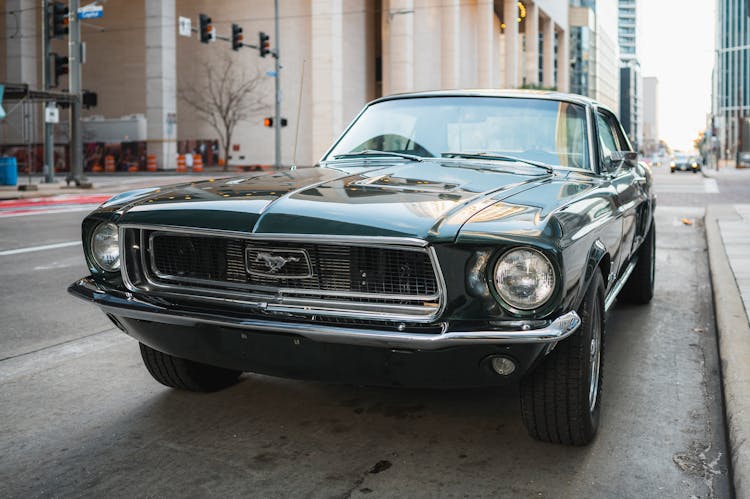 A Green Ford Mustang From The 1960s Parked On A Side Of A Street 