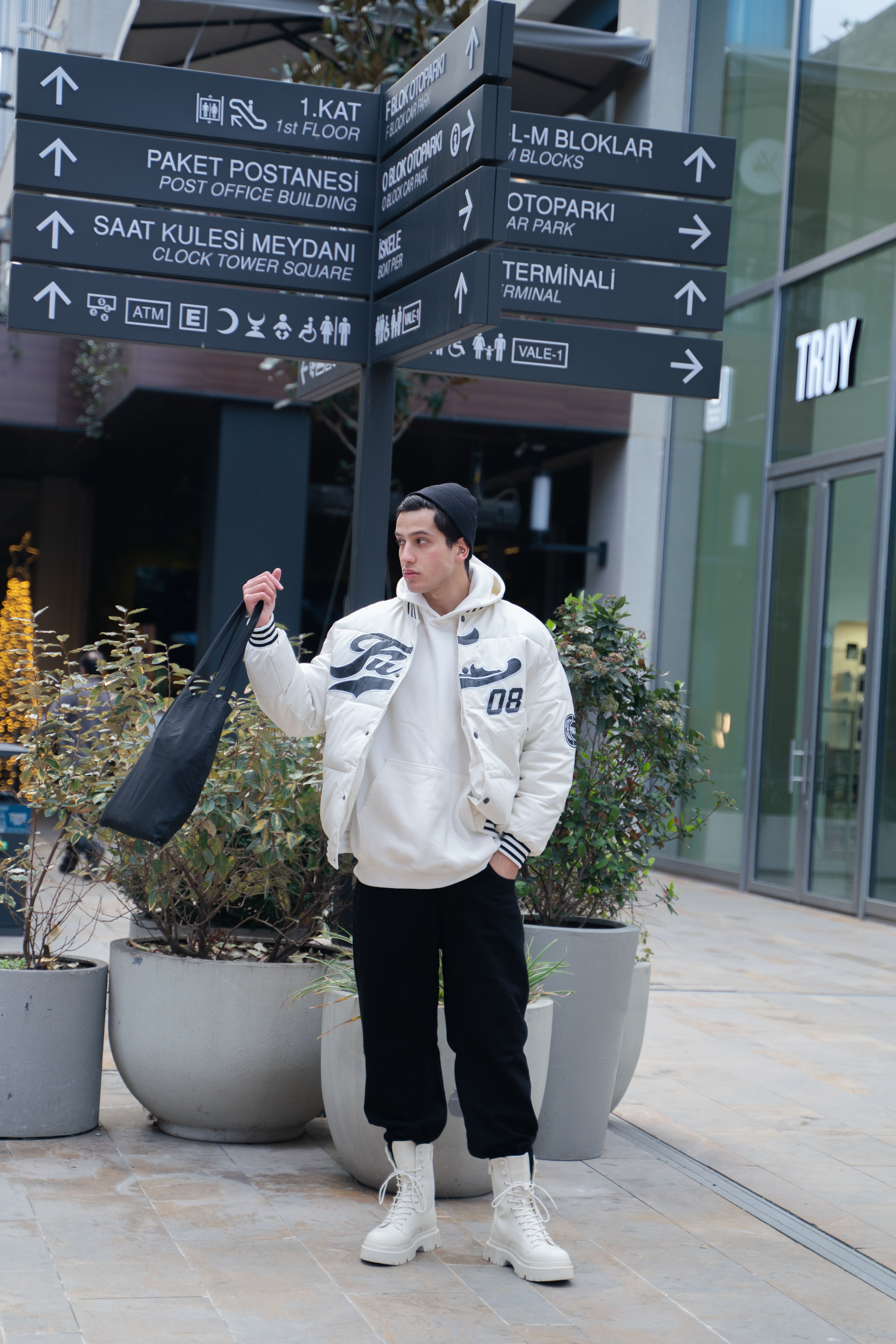 Trendy young man in city street wearing stylish urban wear and holding a bag.