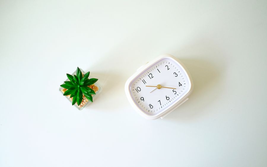A minimalist desk scene with a white clock and a small cactus plant on a white background