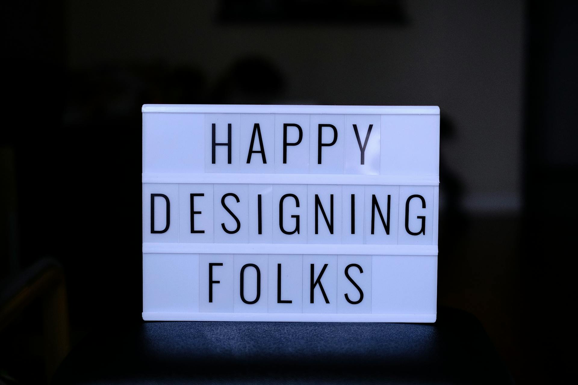 Inspirational lightbox sign reading 'Happy Designing Folks' for creatives and designers.