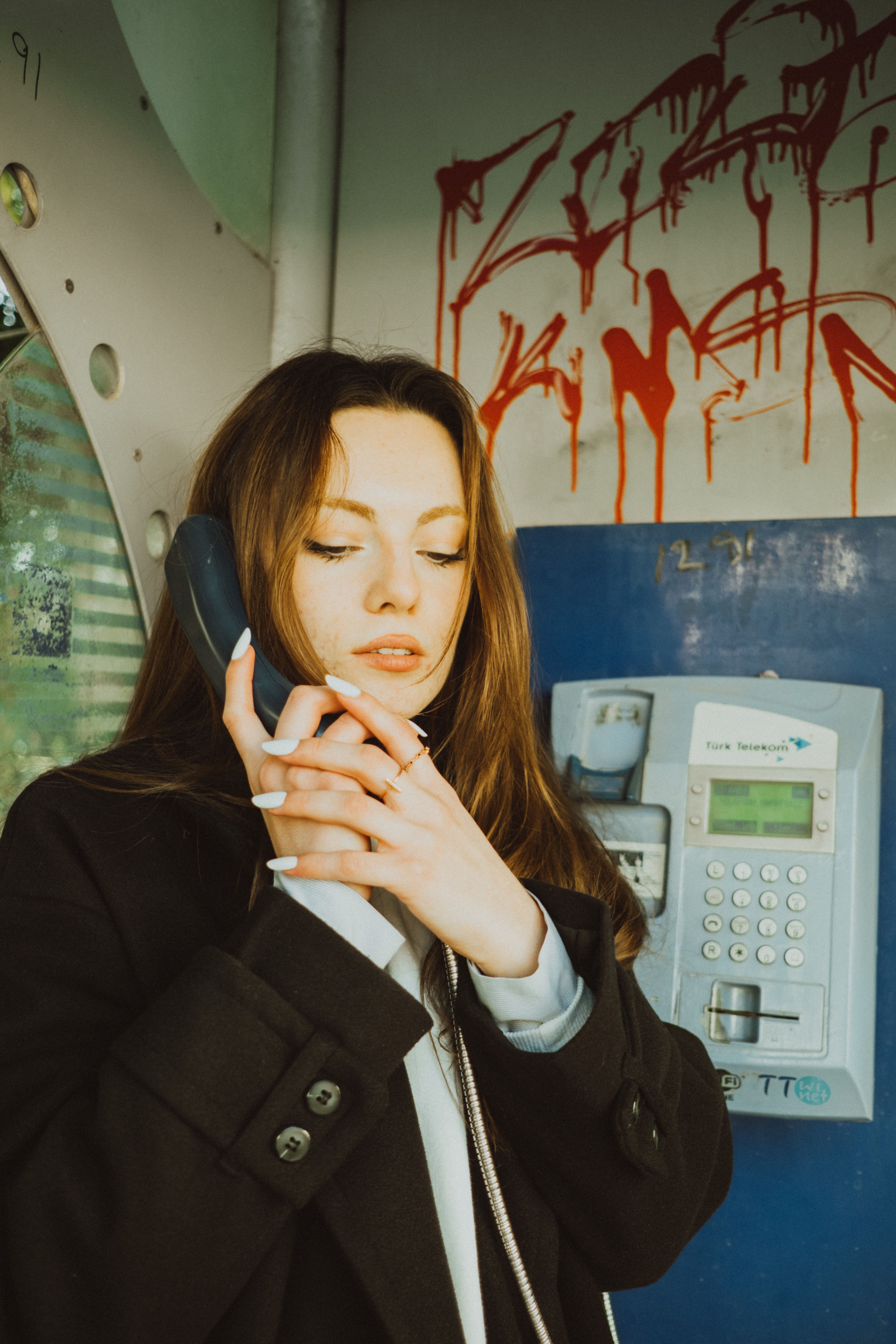 A woman using a retro telephone booth with graffiti, conveying a nostalgic and urban vibe.