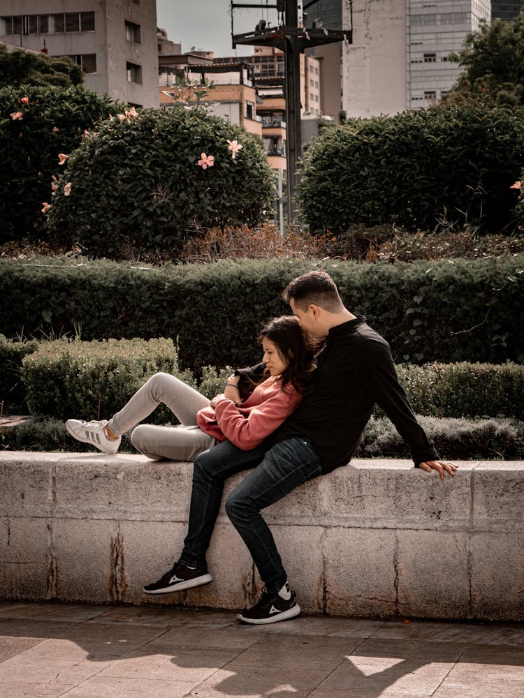 Couple Sitting On Wall In Park