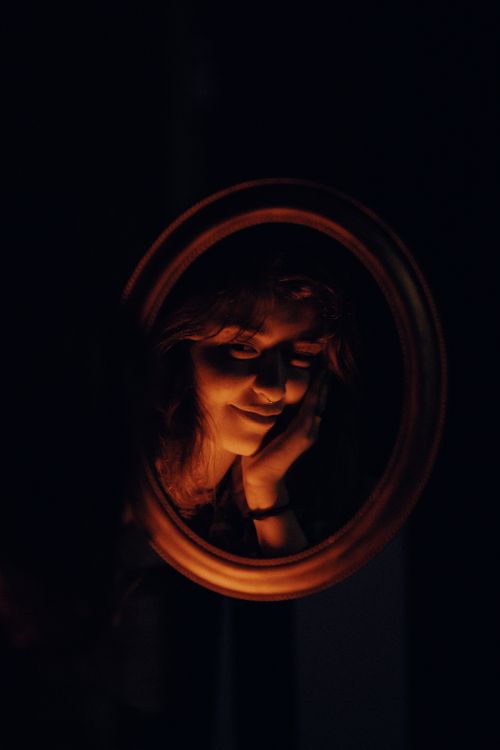 Free A serene portrait of a woman reflected warmly in candlelight within a dark room. Stock Photo