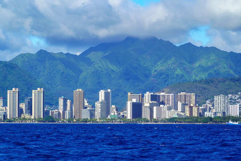 Stunning aerial view of Honolulu's skyline with lush mountains and ocean in foreground.