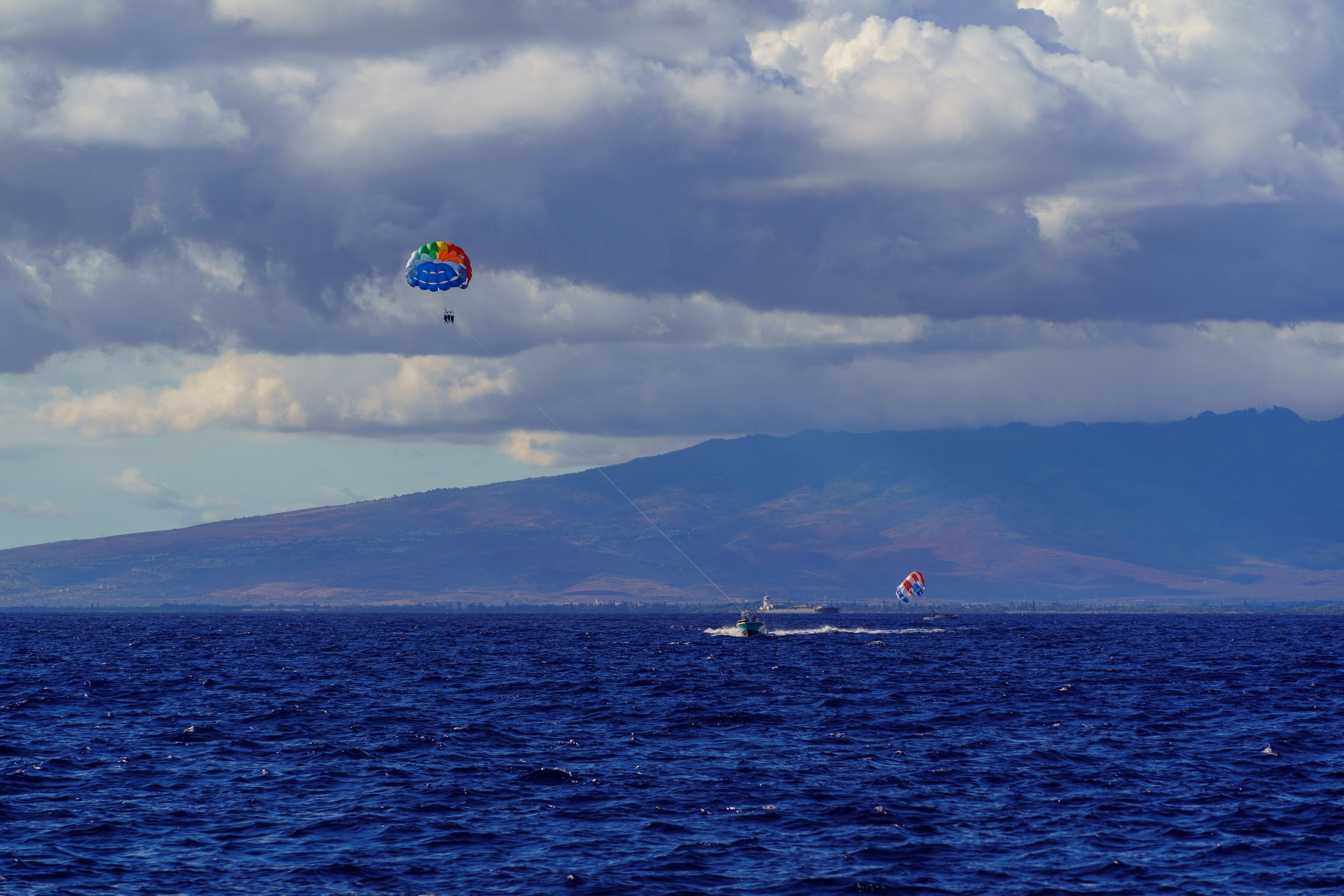 Parasailing adventure over the deep blue sea under a cloud-filled sky and distant coastline.