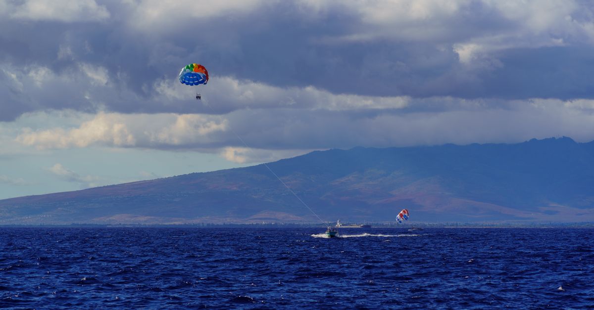 Parasailing adventure over the deep blue sea under a cloud-filled sky and distant coastline.