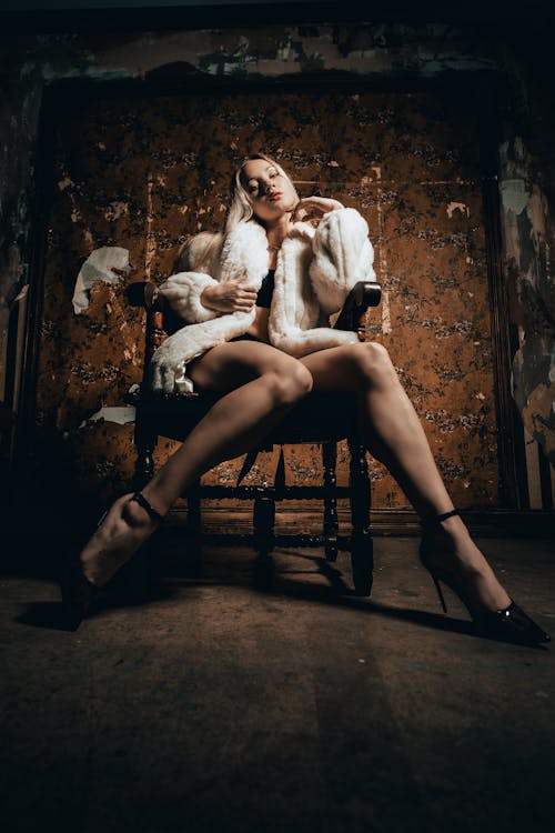 Low Angle View of Woman in Underwear and Fur Coat Sitting in Chair in front of Dirty Wall