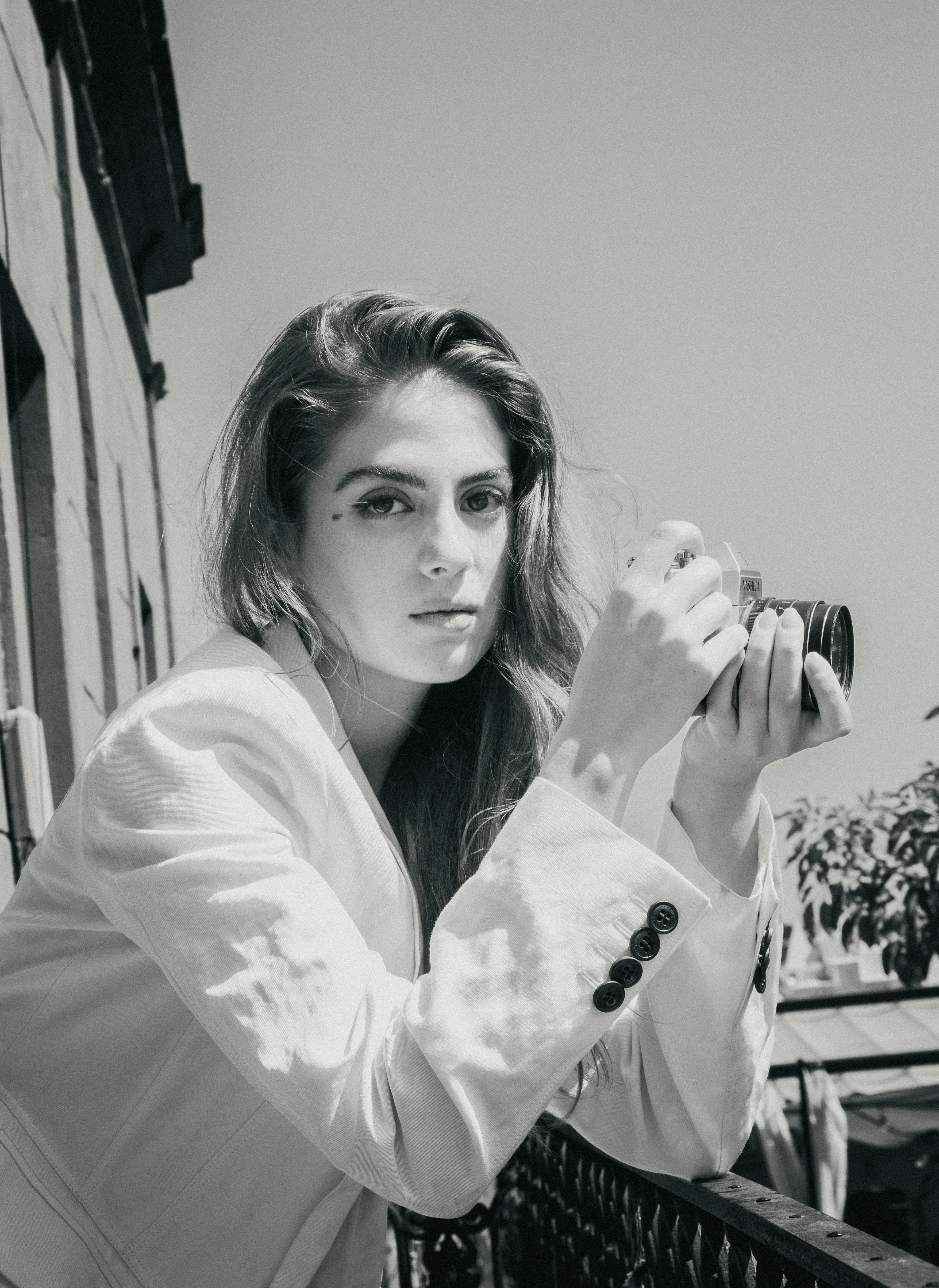 Black and white portrait of a woman in an elegant blazer holding a camera on a balcony in Mexico City.