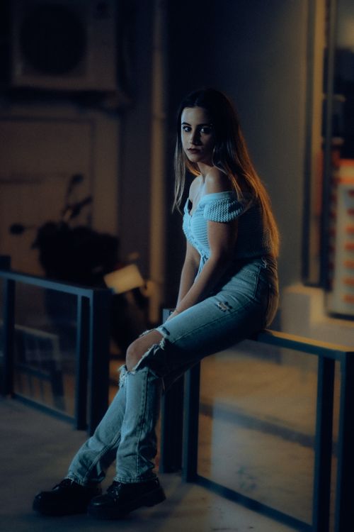 Free Portrait of a young woman sitting on a railing in urban night setting, showcasing a moody vibe. Stock Photo