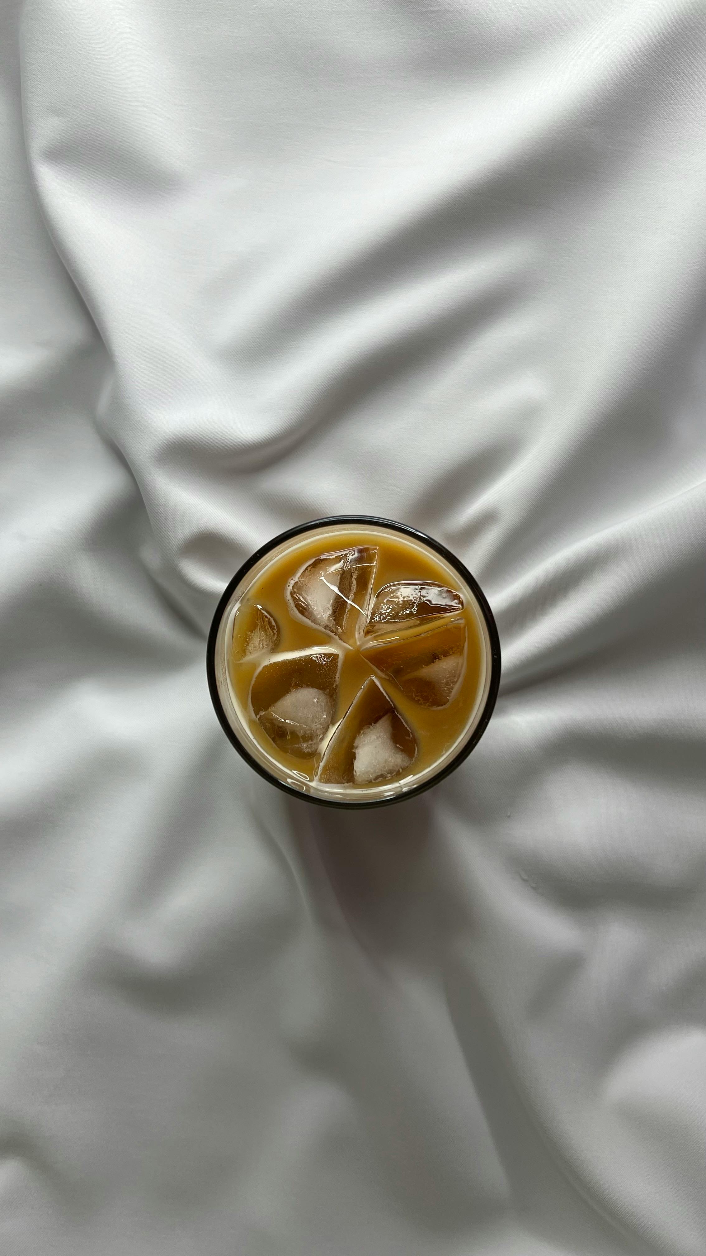 Refreshing iced coffee placed on a luxurious satin sheet viewed from above.
