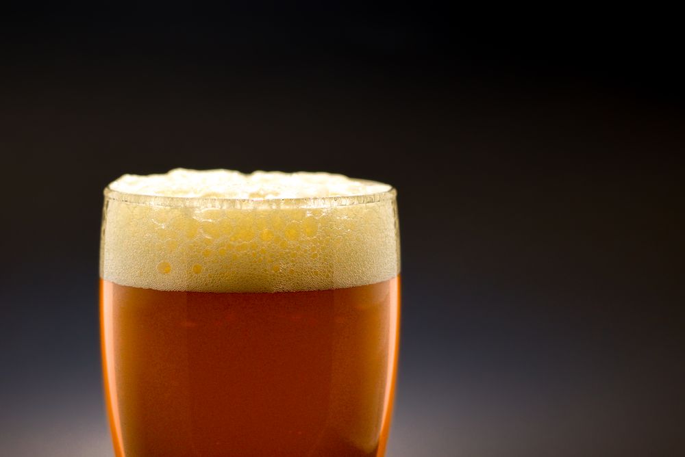 Bicchiere di birra con schiuma su sfondo scuro, immagine stock