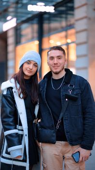 A smiling couple in winter clothing standing together on an urban street.