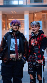 Two young adults showcasing alternative fashion styles standing on a city street.
