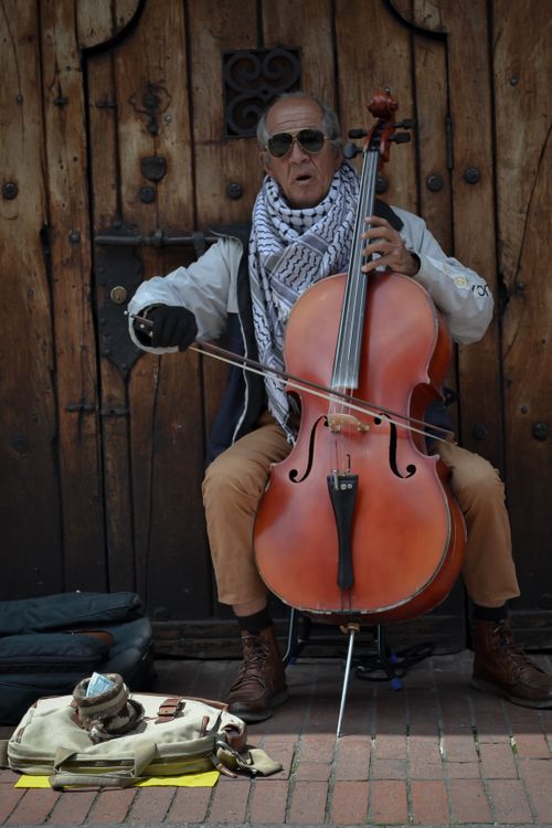 Free Senior musician performing cello on a historic city street, showcasing passion and skill. Stock Photo