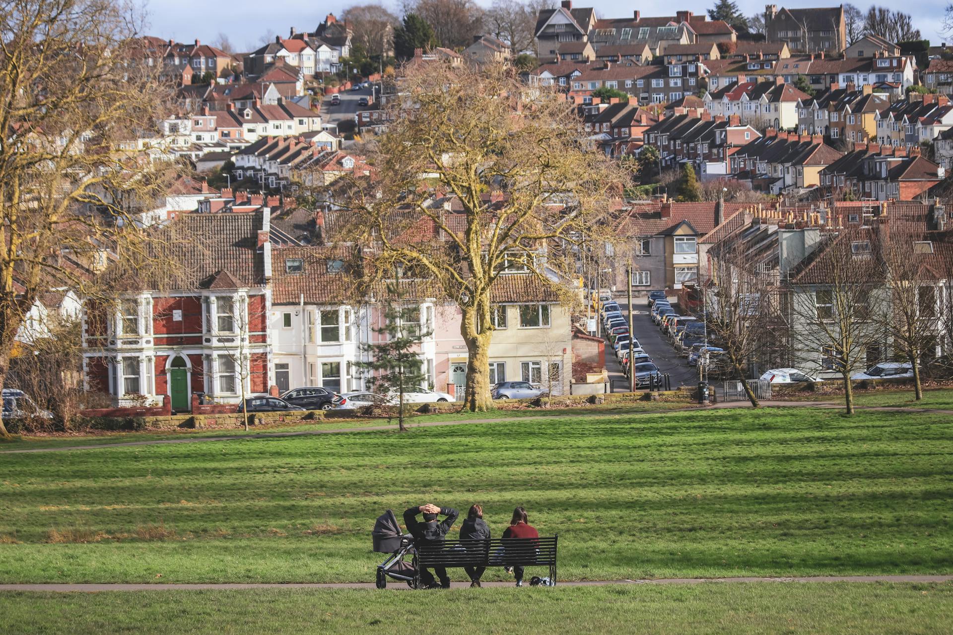 A serene scene of people relaxing on a bench in a Bristol park with cityscape in the background.
