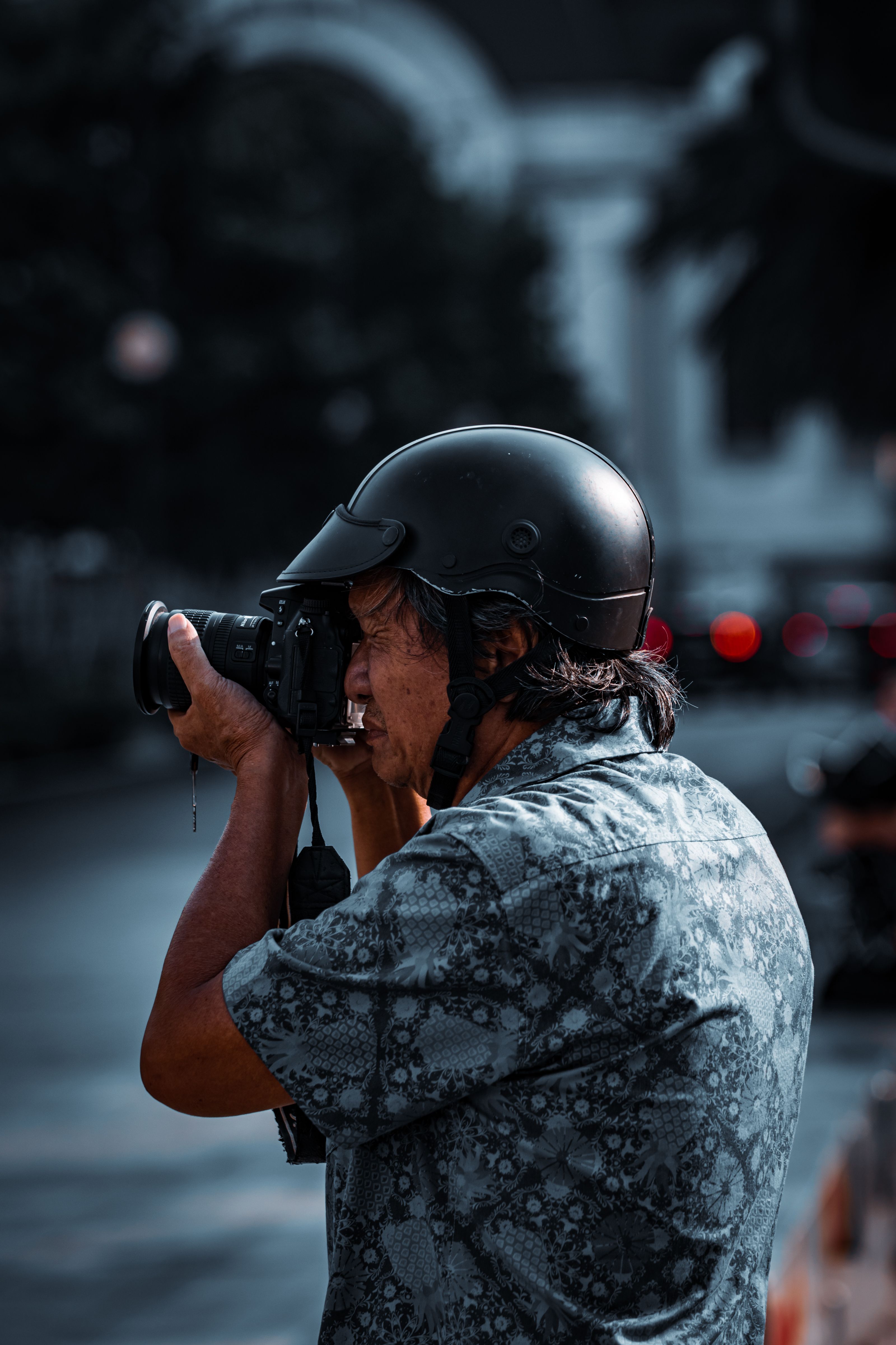 Photographer in a helmet capturing city street scene with a professional camera on a cloudy day.
