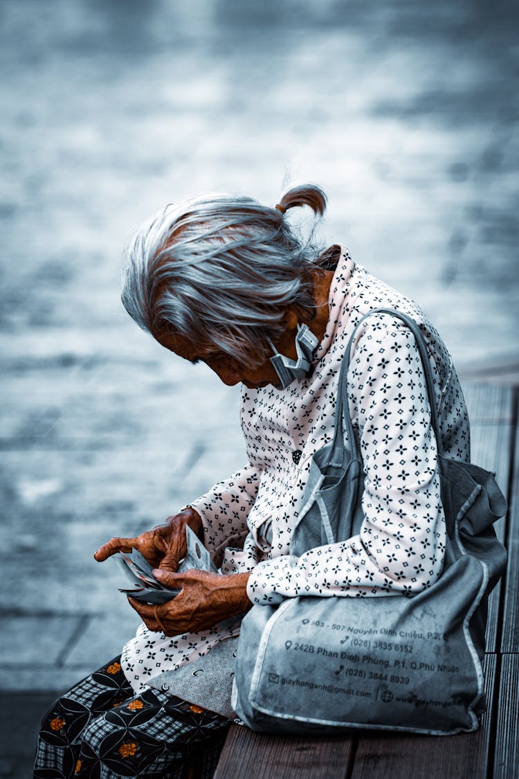 Elderly Woman Counting Money On A Bench 