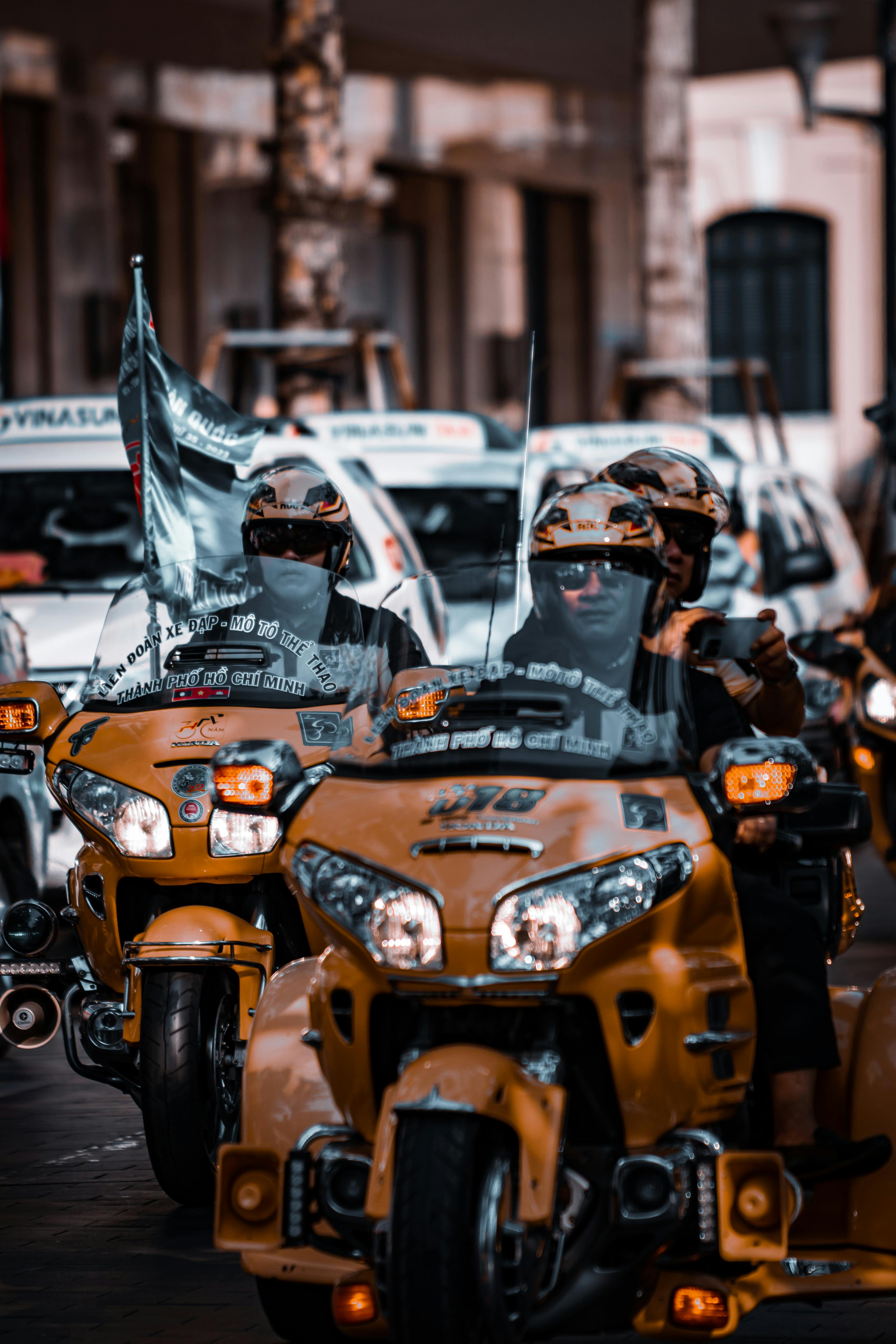 Motorcyclists with flags participating in a vibrant urban street rally on bright yellow bikes.
